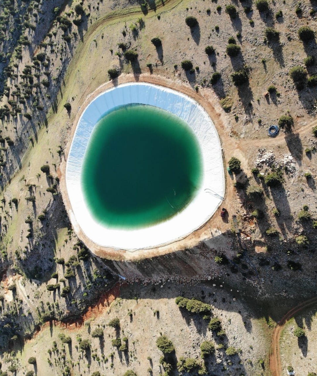 Aerial view of a lined artificial irrigation lake in a mountainous landscape
